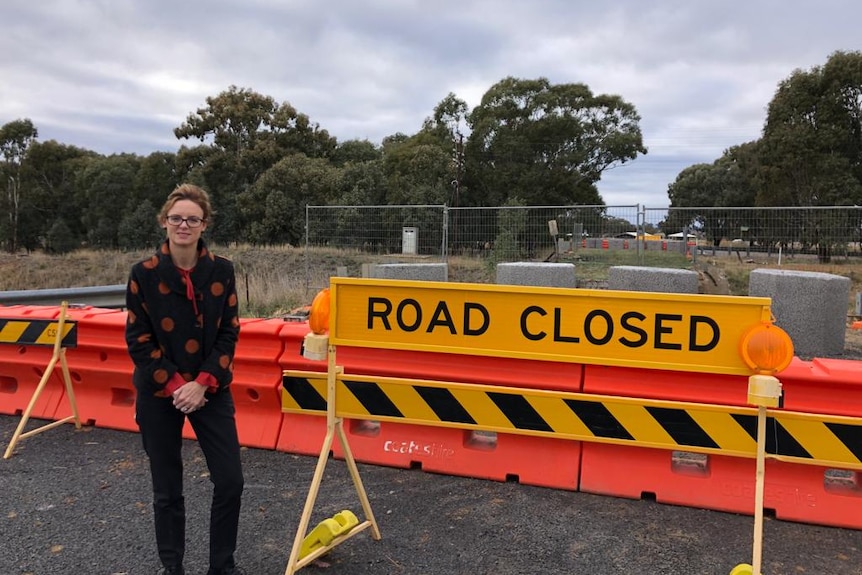 A middle-aged woman stands in front of a road closure sign.