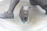 A metal statue of a cat next to a man's foot