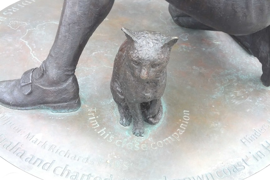 A metal statue of a cat next to a man's foot