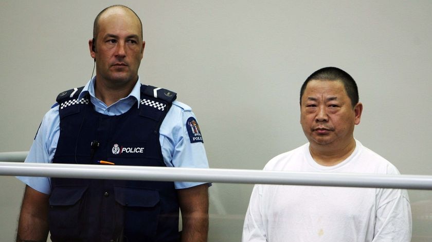 Michael Xue is flanked by a police officer as he stands in the dock