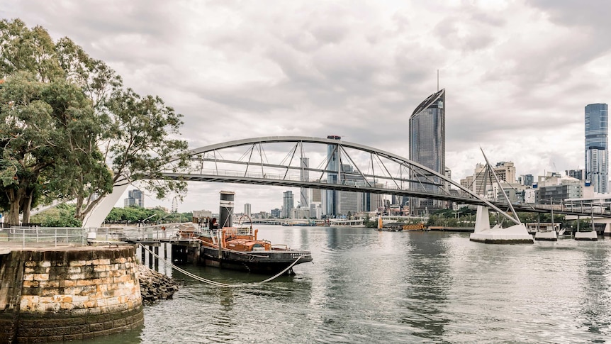 An old boat docked along the Brisbane River at South Brisbane. The Goodwill Bridge links South Brisbane to the city centre.