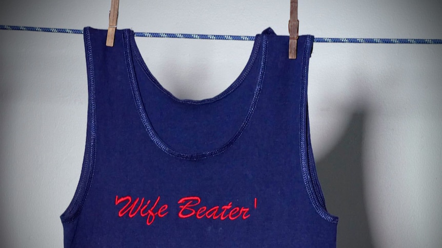 A blue singlet hanging by pegs on a clothes line, embroidered with the words 'wife beater'.