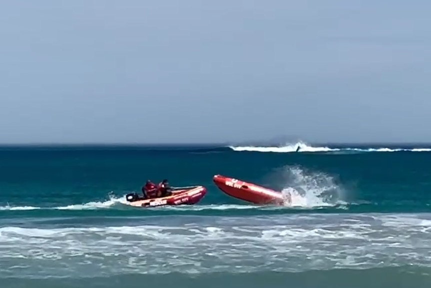 two men in an inflatable boat approach another one without a driver on the sea