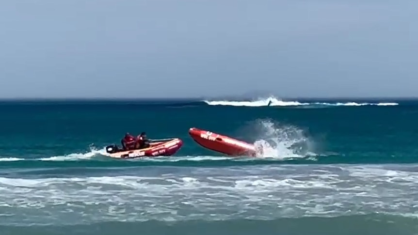 two men in an inflatable boat approach another one without a driver on the sea