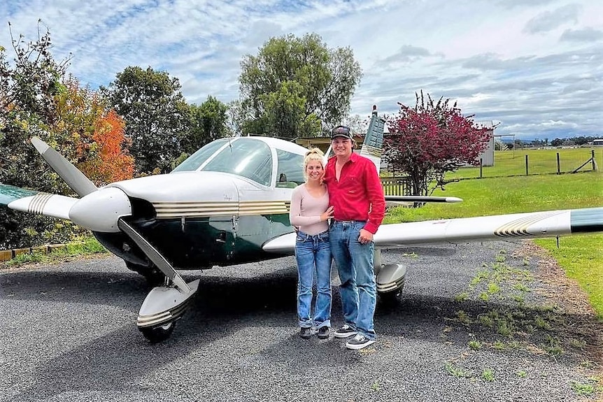 A young man and woman standing together in front of a light plane.