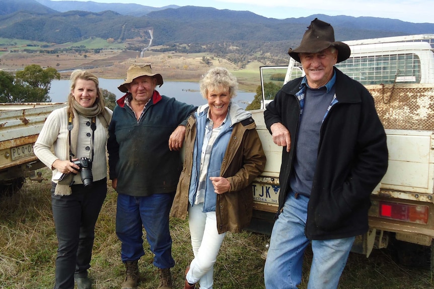 Brigid Donovan holding stills camera, locals 'Snags', Heather Ewart and 'Dougie' standing at back of ute with mountains behind.