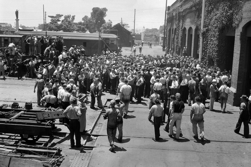 black and white photo, men gathered en masse outside workshops