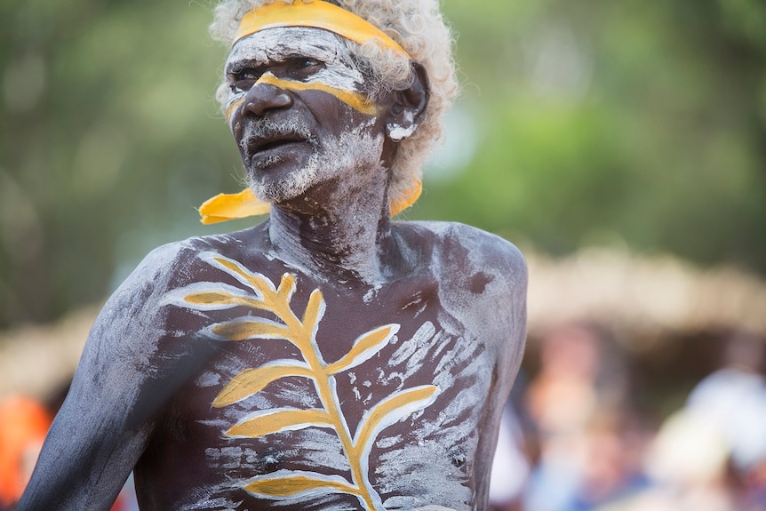 Eddie William Gumbula wears white and yellow body paint and looks away from camera