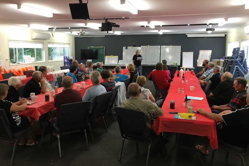 A woman speaks to a crowd of people sitting at long tables.