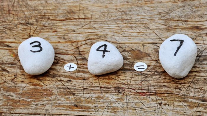 The sum 3 + 4 = 7 is spelled out on pebbles