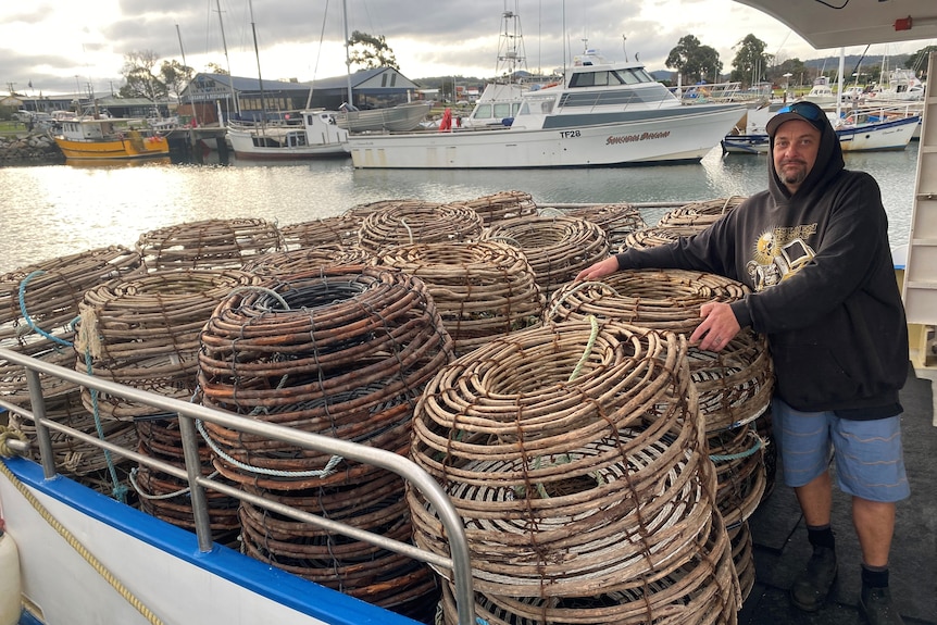 A man stands next to piles of cray pots on a fishing boat.