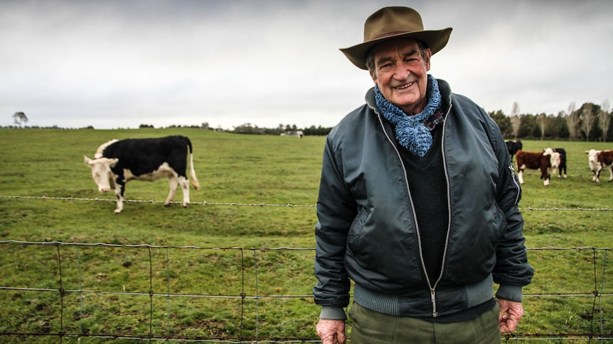 Retired farmer Noel Jenner standing in front of a fence with cows in the background.