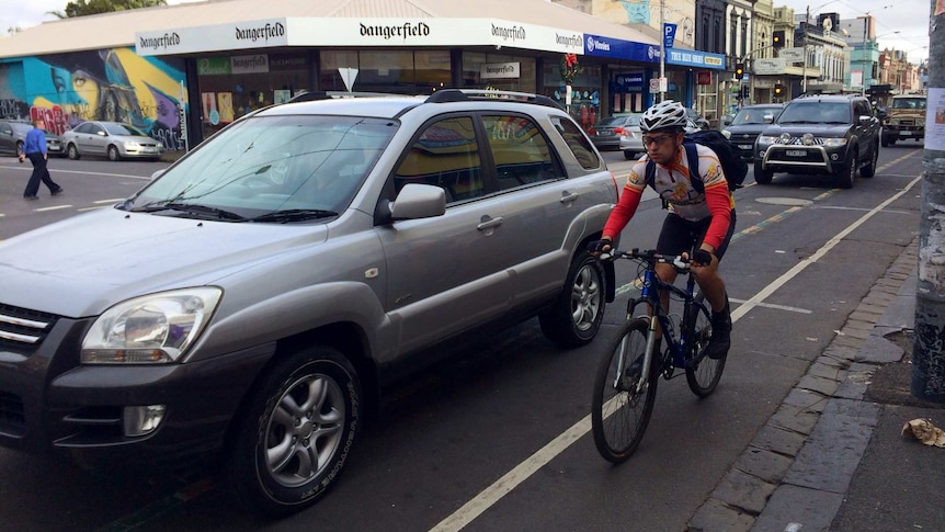 A car passes close by a cyclist on Sydney Road in Brunswick.