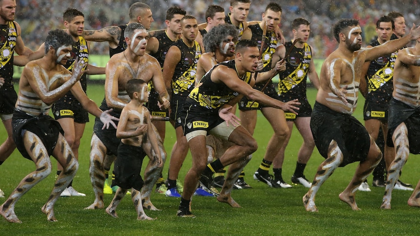 Sydney Stack is front and centre, surrounded by painted Indigenous men and followed by his teammates, doing a traditional dance
