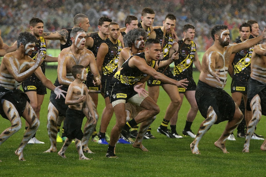 Sydney Stack is front and centre, surrounded by painted Indigenous men and followed by his teammates, doing a traditional dance