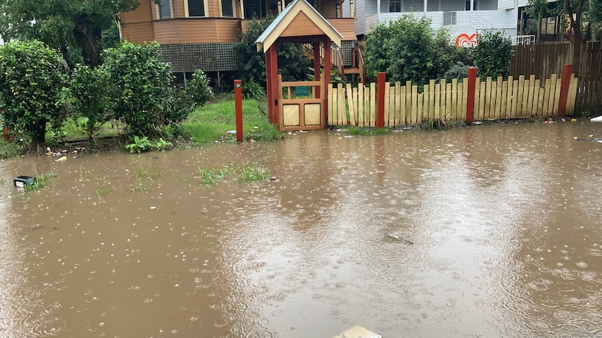 brown flash flood pools in front of wood picket fence, raised house in the background.