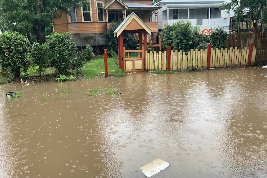 brown flash flood pools in front of wood picket fence, raised house in the background.