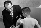 Black and white photo of Dr Jonas Salk injecting the polio vaccine into a young boy's arm.
