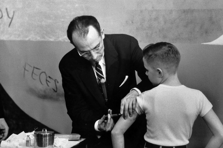 Black and white photo of Dr Jonas Salk injecting the polio vaccine into a young boy's arm.