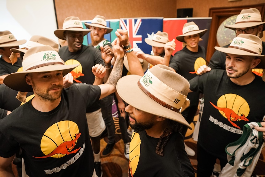 Boomers players wearing Akubras put their hands together in a team huddle.