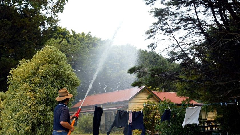 A resident of Kinglake hoses down his house in preparation for approaching bushfires