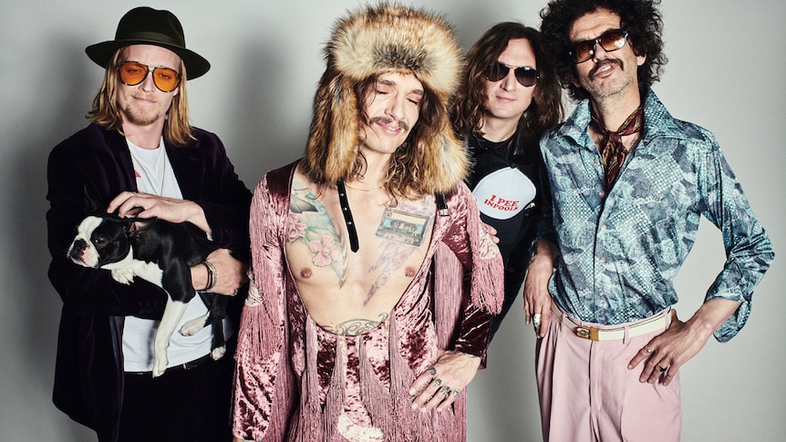 One member of The Darkness holds a dog, one has his shirt open and wears a hunting cap, three wear sunglasses