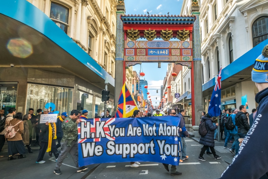 Looking down a narrow Melbourne street, you view a crowd of people holding anti-China banners and Australian flags.