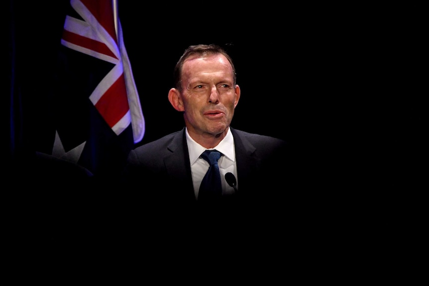 A man stands in the spotlight at a lectern.