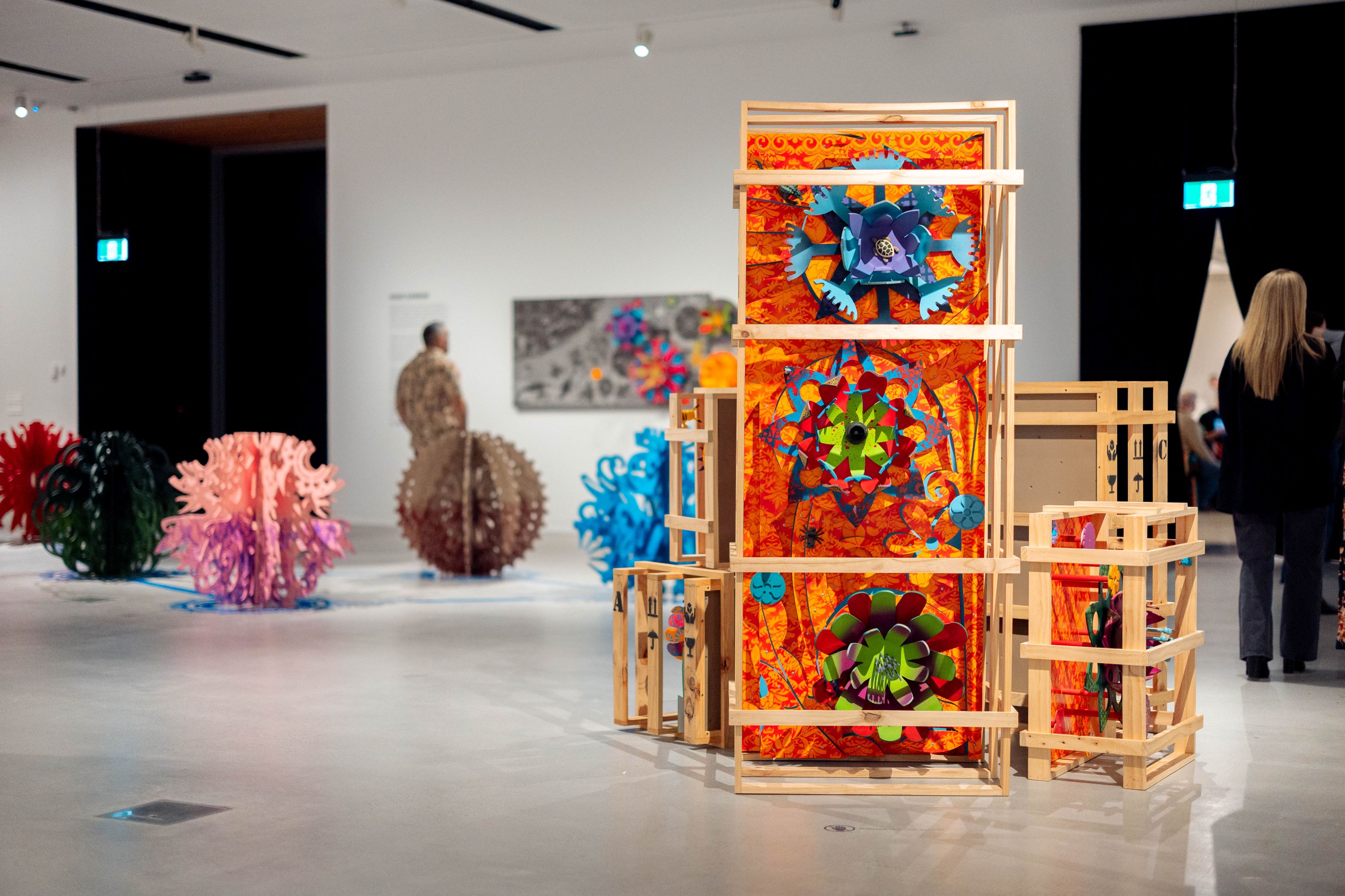 Una gran escultura con elementos coloridos, exhibida en cajas de madera apiladas, en una galería de arte.