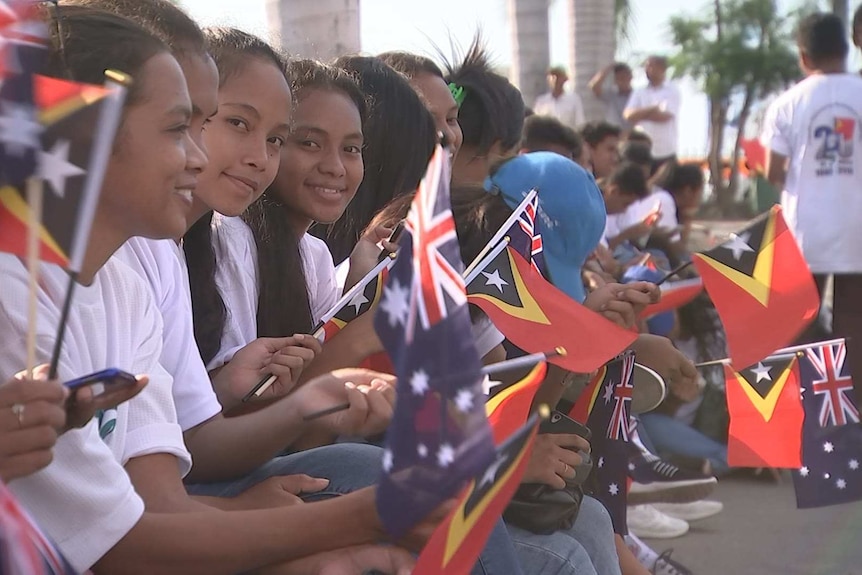 A row of girls wave Timorese and Australian flags, some looking at the camera