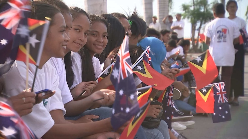 A row of girls wave Timorese and Australian flags, some looking at the camera