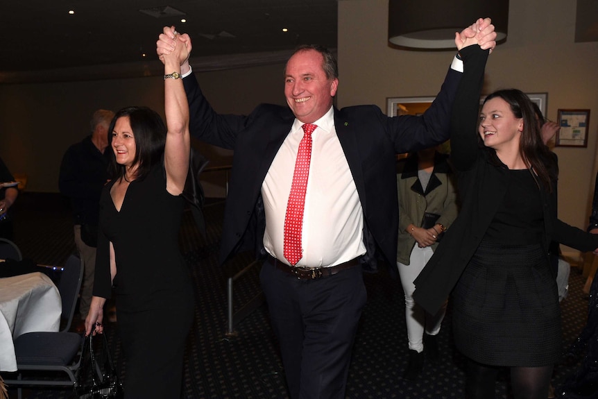 Barnaby Joyce grins while holding the hands of his wife and one of his daughters up in the air.