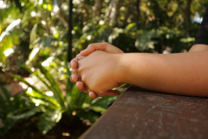 A person folds their hands leaning on a balcony.