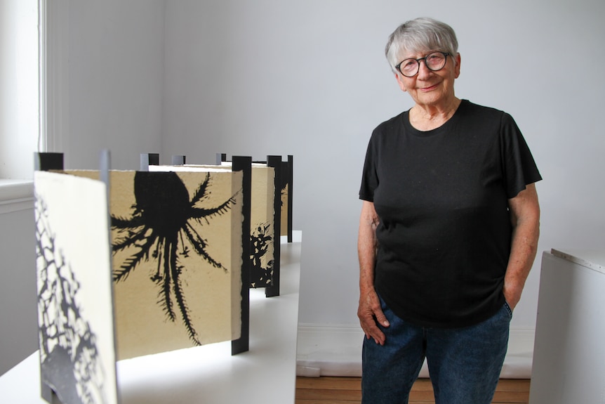 A woman stands beside her handmade book on display.