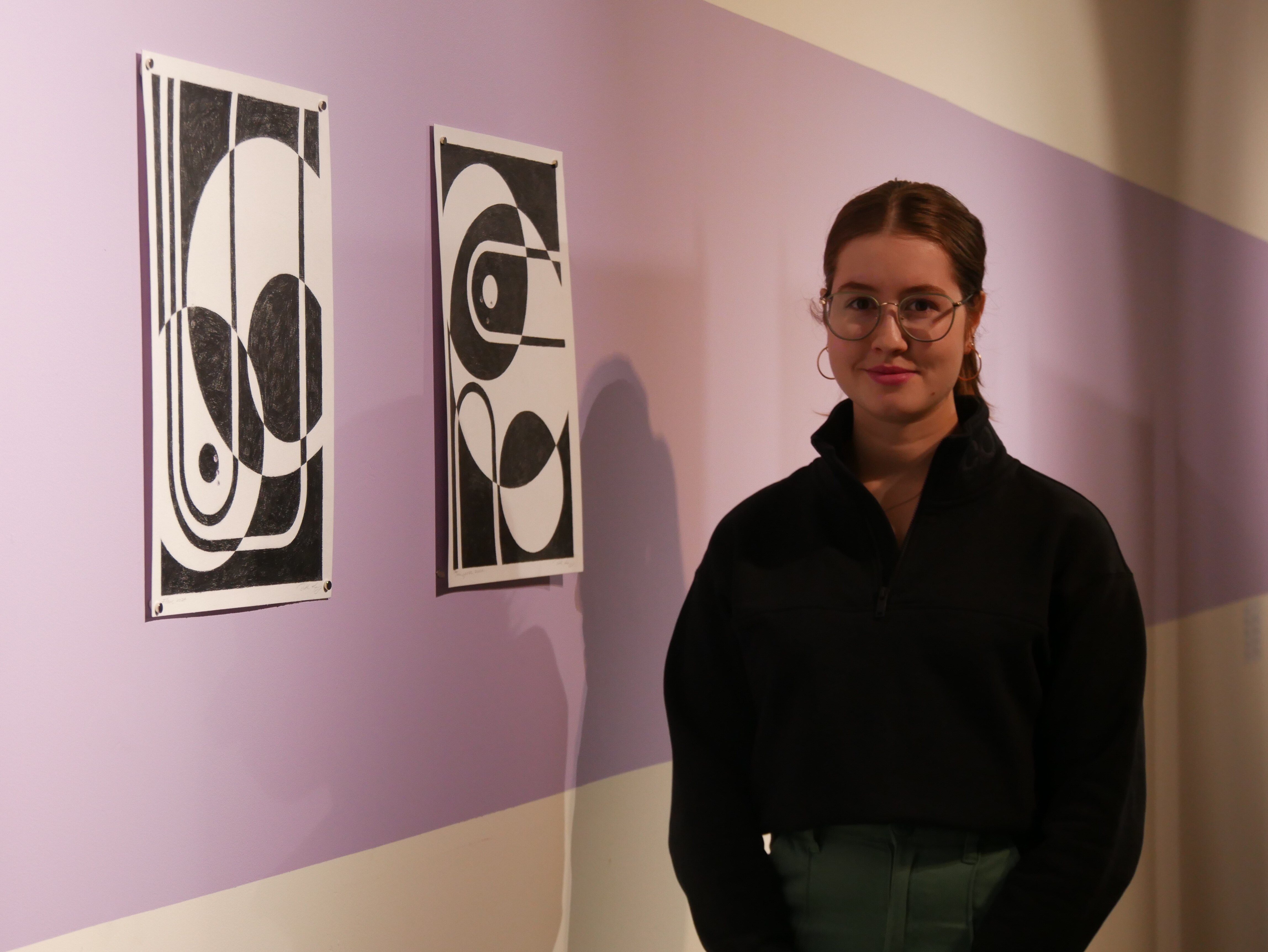 Молодой художник стоит рядом с двумя своими работами.