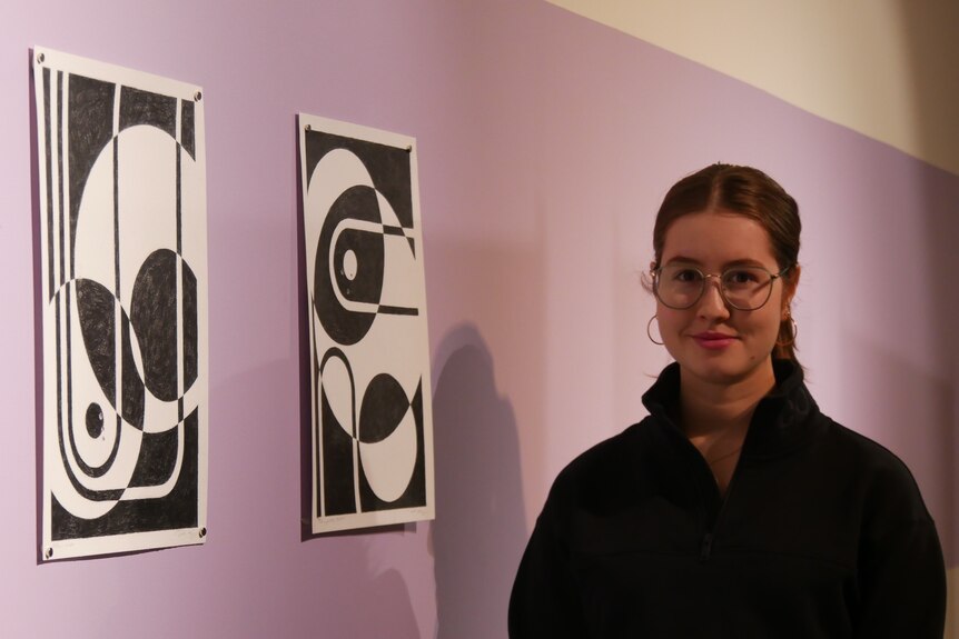 A young female artist standing next to two of her works
