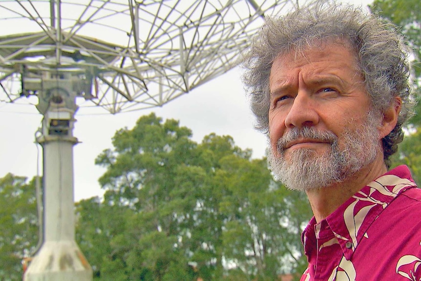 A man stands with a telescope in the background.