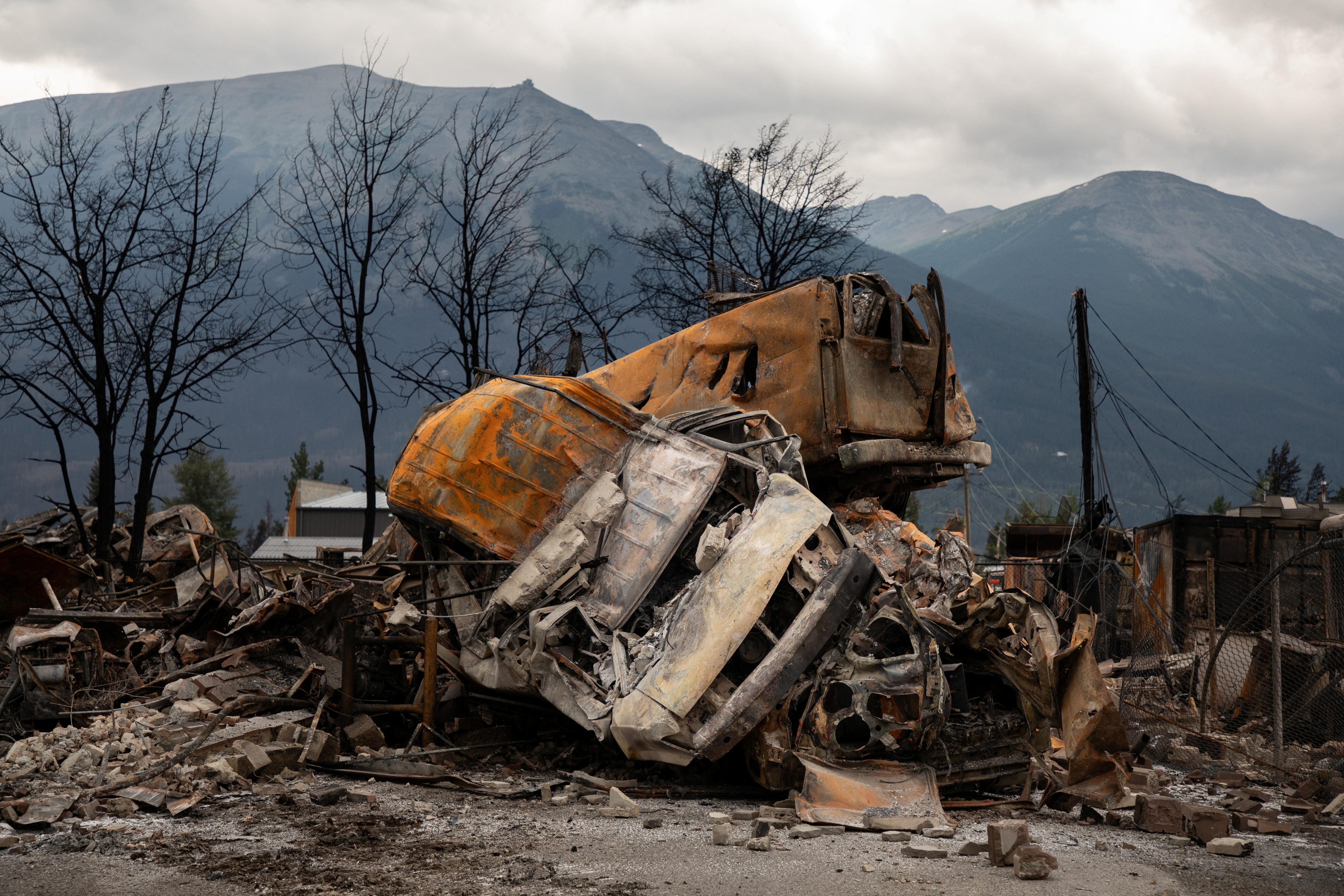 A grey and a yellow car sit on top of each other barely indistinguishable in a pile of ash and wreckage