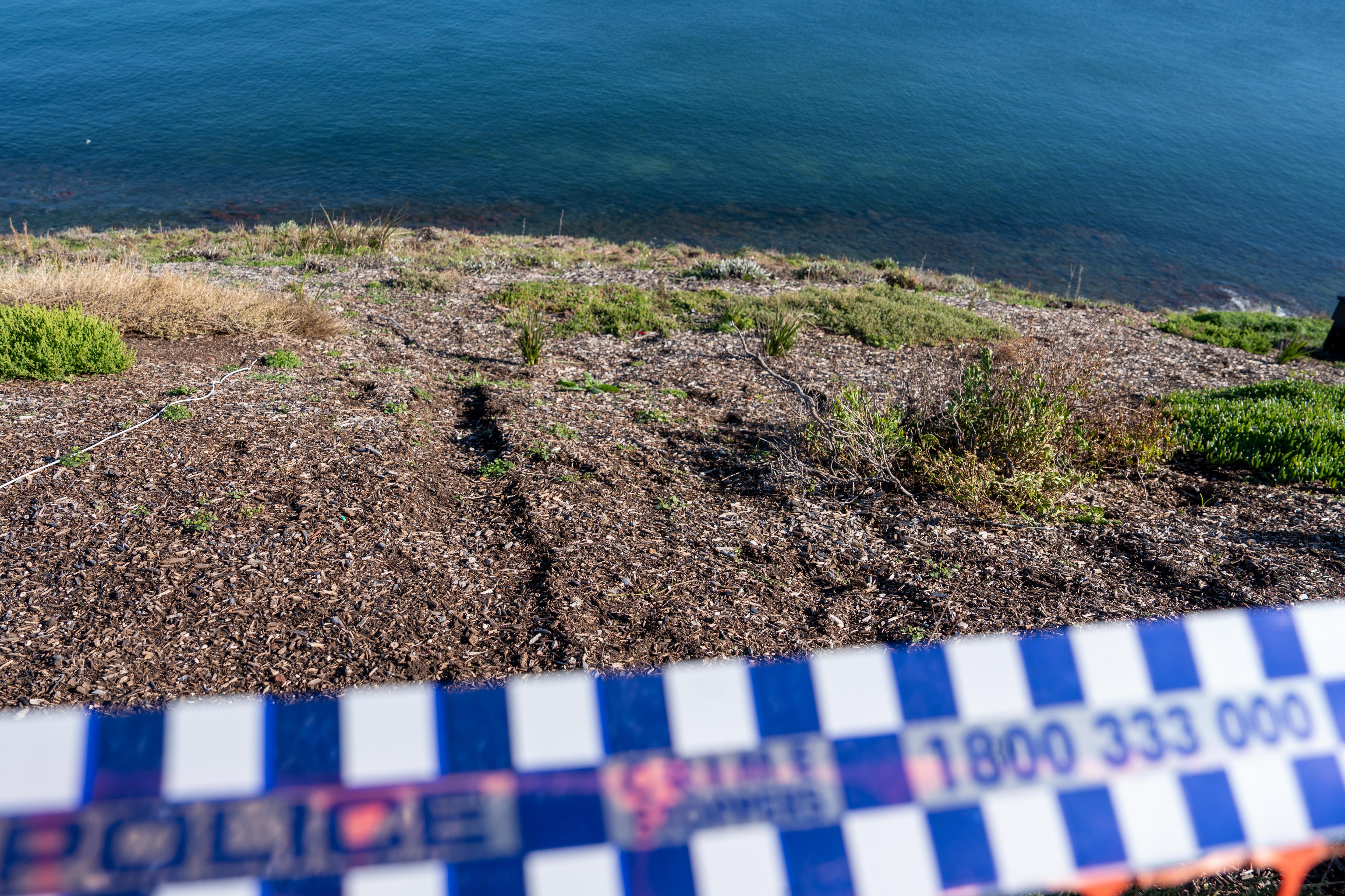 Police tape sectioning off soil showing two distinct tyre marks on a cliff face with some grass