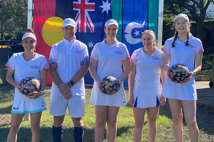 Umpires hold balls with Indigenous art as they stand in front of the Aboriginal, Australian and Torres Strait Islander flag