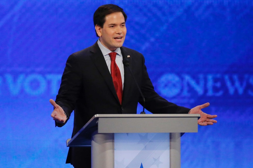 A man in a suit speaking at a debate.