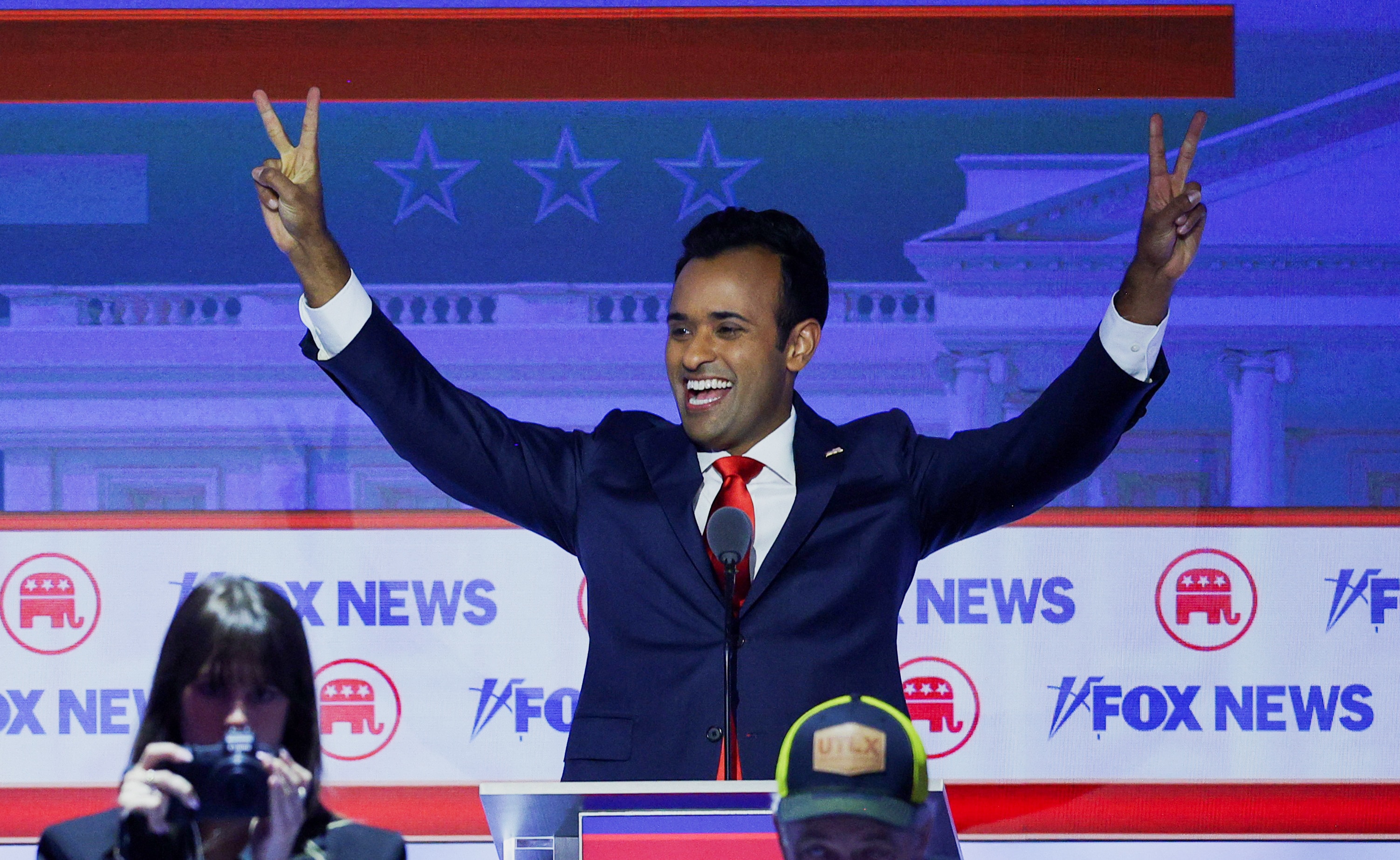 A man in a suit raises his hands and gives two peace signs 