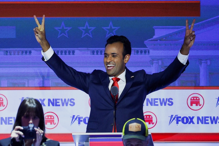A man in a suit raises his hands and gives two peace signs 
