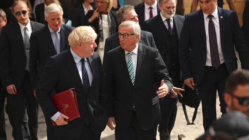 Boris Johnson stands in a crowd speaking with Jean-Claude Juncker, as they leave a restaurant in Luxembourg.