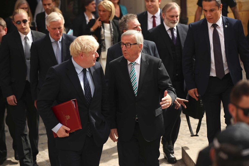 Boris Johnson stands in a crowd speaking with Jean-Claude Juncker, as they leave a restaurant in Luxembourg.