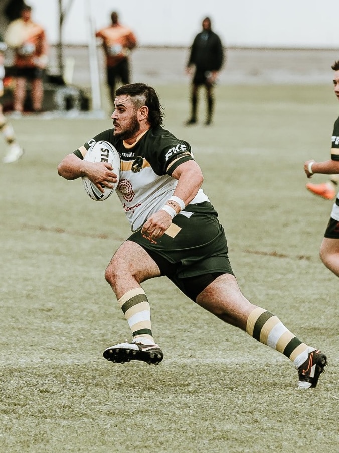 A man with black hair and a green jersey running holding a rugby league ball