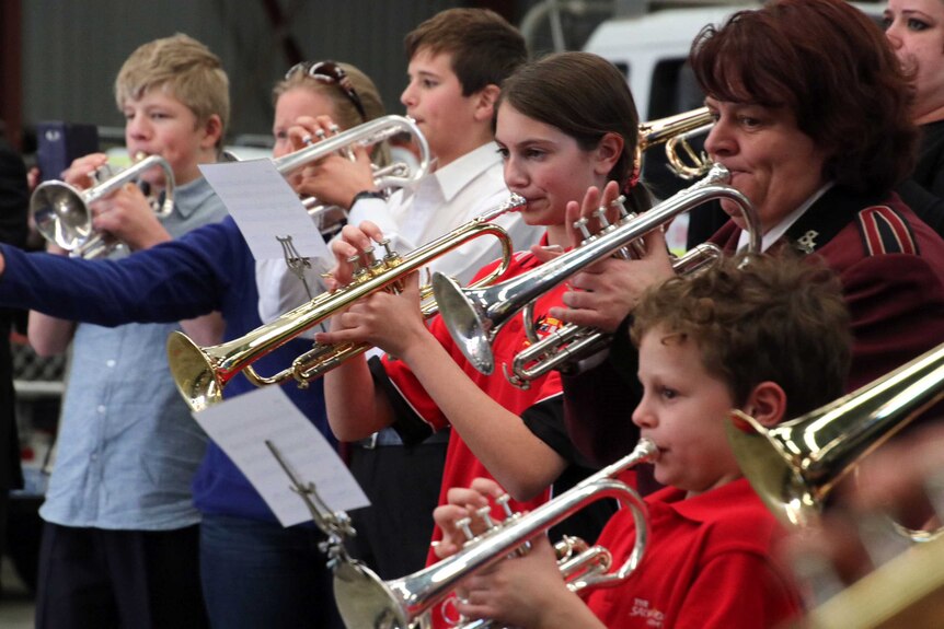 Children and adults play the bugle in a line.