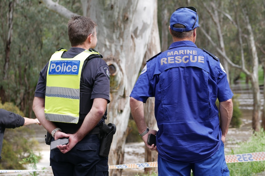 Police and marine rescue officers stand in front of flooded bushland.
