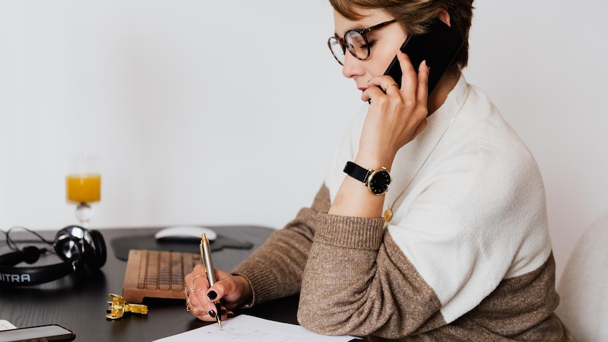 A woman holds a phone to her ear while holding a pen.