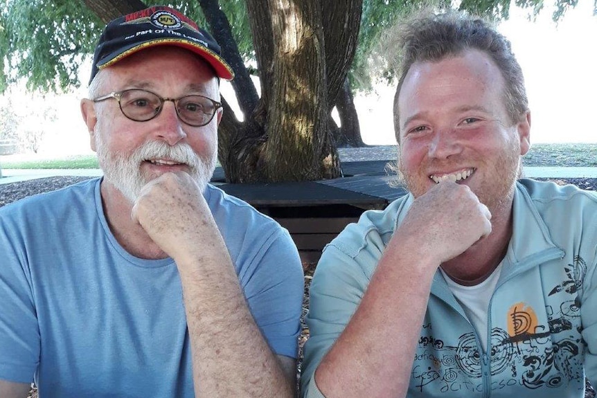 Matty Wright poses for a photo sitting to the left of biological father Alan in a park during daytime.